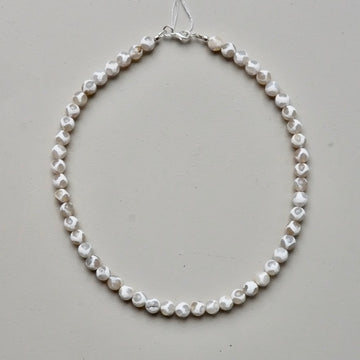 A single-strand necklace made of irregular, faceted white shell beads, displayed on a neutral light gray background.