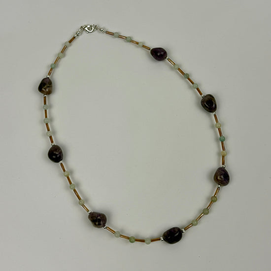 Necklace with dark beads and gold beads on a light grey background