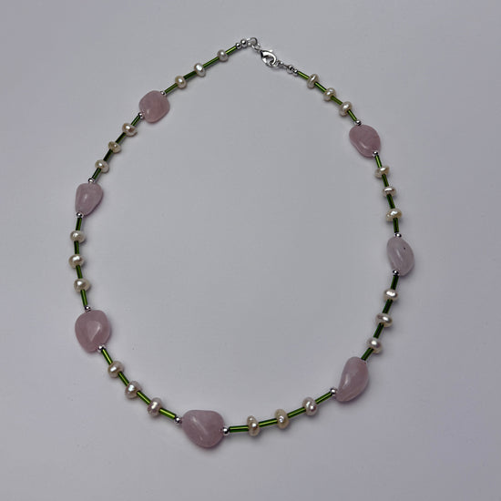 Necklace with pink shaped beads and green and silver chain on a light gray background