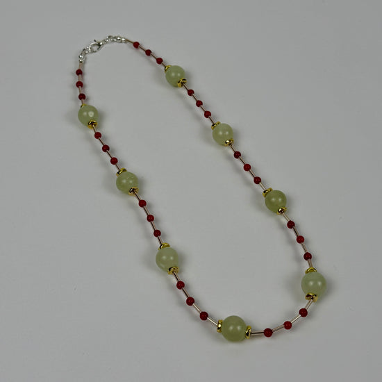Necklace with green beads and red accents on a grey background