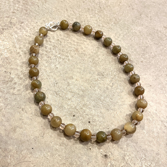 Beaded necklace with green and clear pink beads on a light grey concrete surface