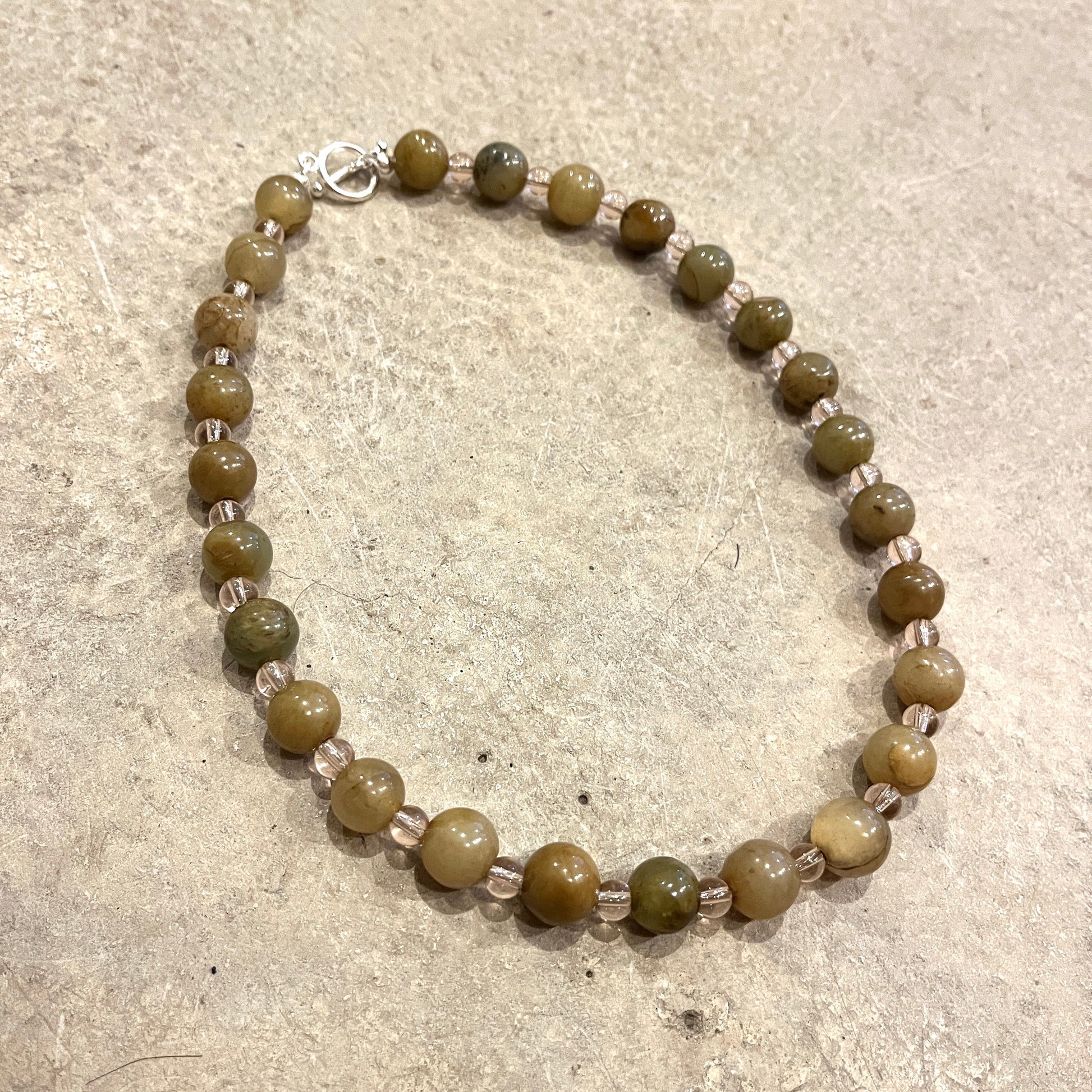 Beaded necklace with green and clear pink beads on a light grey concrete surface