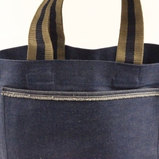Blue denim tote bag with striped handles on a white background