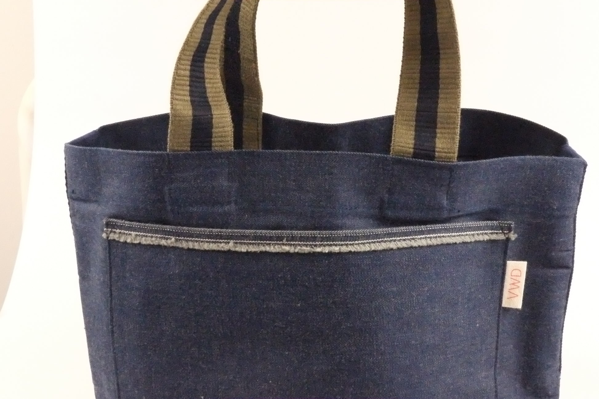 Blue denim tote bag with striped handles on a white background