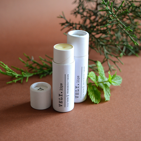 Two white lip balm containers with green leaves on a brown background