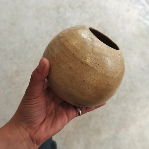 Hand holding a small brown ceramic vase against a neutral background