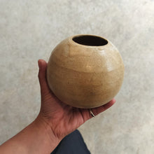 Load image into Gallery viewer, Hand holding a spherical beige ceramic vase on a light gray background
