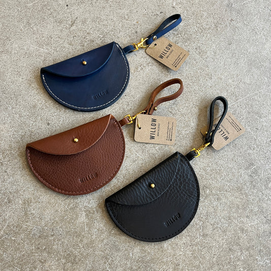 Three leather keyring purses in black, brown, and blue colors, displayed on a textured surface, each with a tag showing the brand name 'Willow Leather'.