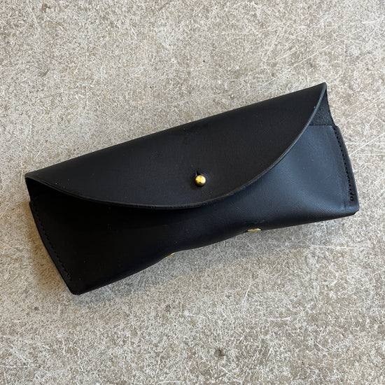 Four leather sunglasses cases in different colors (black, brown, tan) laid out on a textured surface.