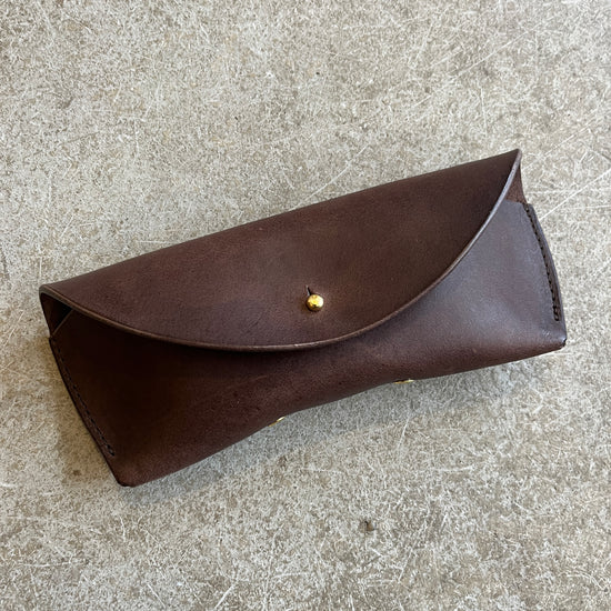 Four leather sunglasses cases in different colors (black, brown, tan) laid out on a textured surface.