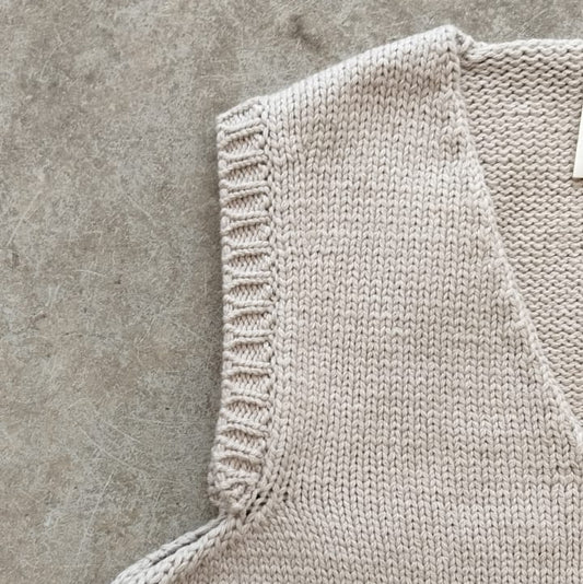 Close-up of a beige knitted sleeveless garment on a concrete surface