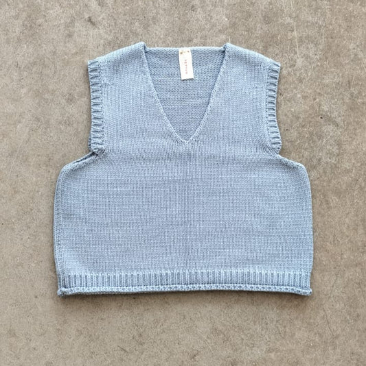 Light blue knitted vest on a beige surface