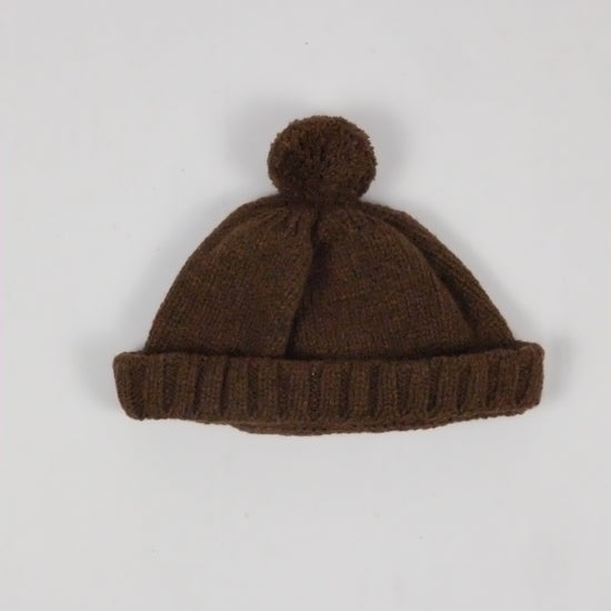 Brown knit beanie with pom-pom on a light gray background