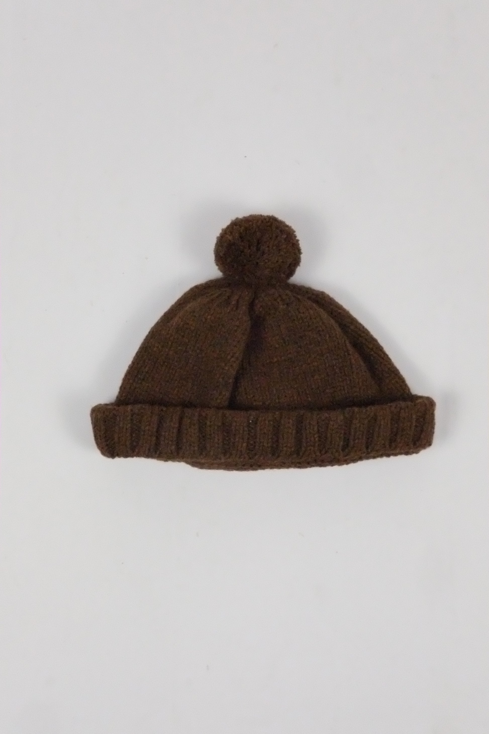 Brown knit beanie with pom-pom on a light gray background