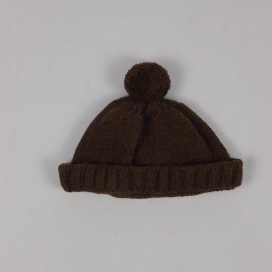 Brown knit beanie with pom-pom on a light gray background
