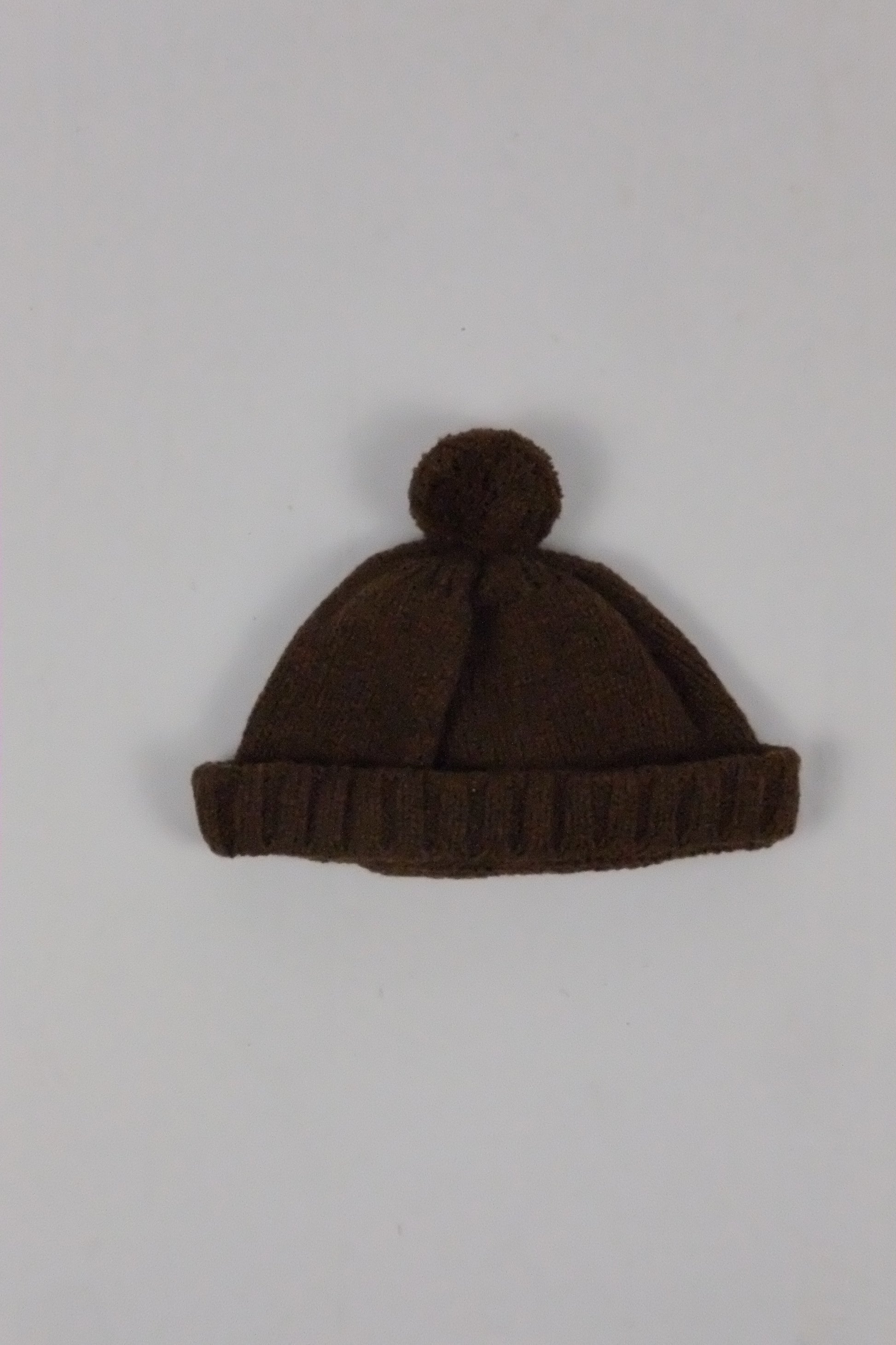 Brown knit beanie with pom-pom on a light gray background