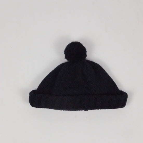 Black knit beanie with pom-pom on a light gray background