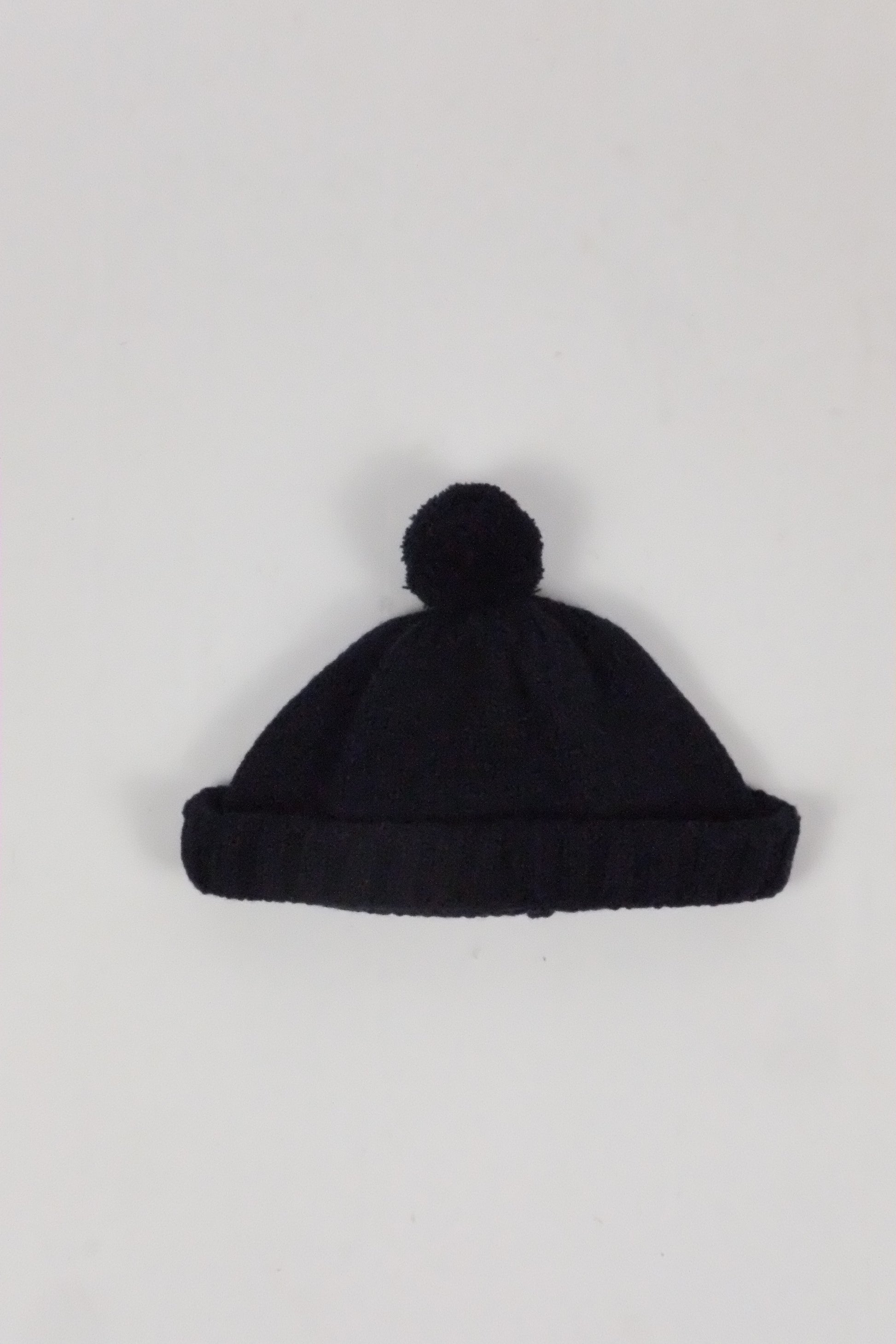 Black knit beanie with pom-pom on a light gray background
