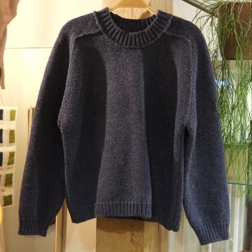 A dark navy knit sweater with a crew neck and ribbed cuffs and hem, hanging on a wooden hanger on a clothing rack inside a store.
