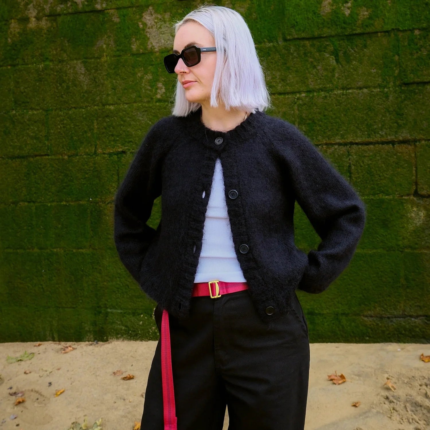 Woman standing by a green wall wearing a black cardigan