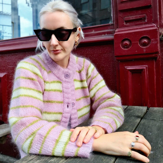 Woman wearing a pink and green striped sweater sitting outdoors.