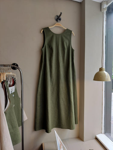 Green linen sleeveless dress hanging on a hanger against a neutral wall.
