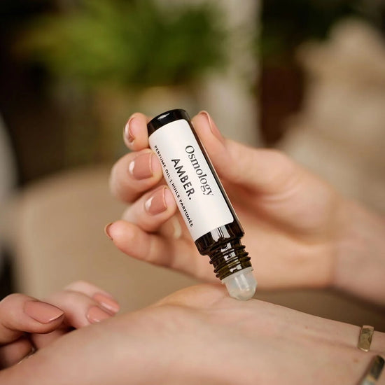 Person applying a small rollerball bottle to their wrist with a blurred background