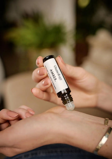 Person applying a small rollerball bottle to their wrist with a blurred background