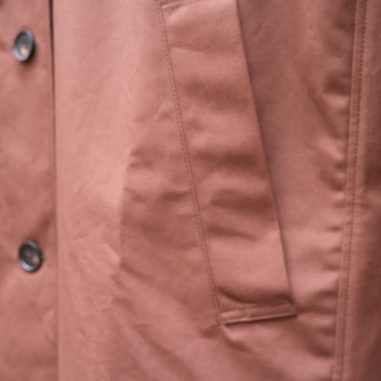 Close-up of a chocolate brown jacket fabric, showing a vertical welt pocket and part of a buttoned front closure.