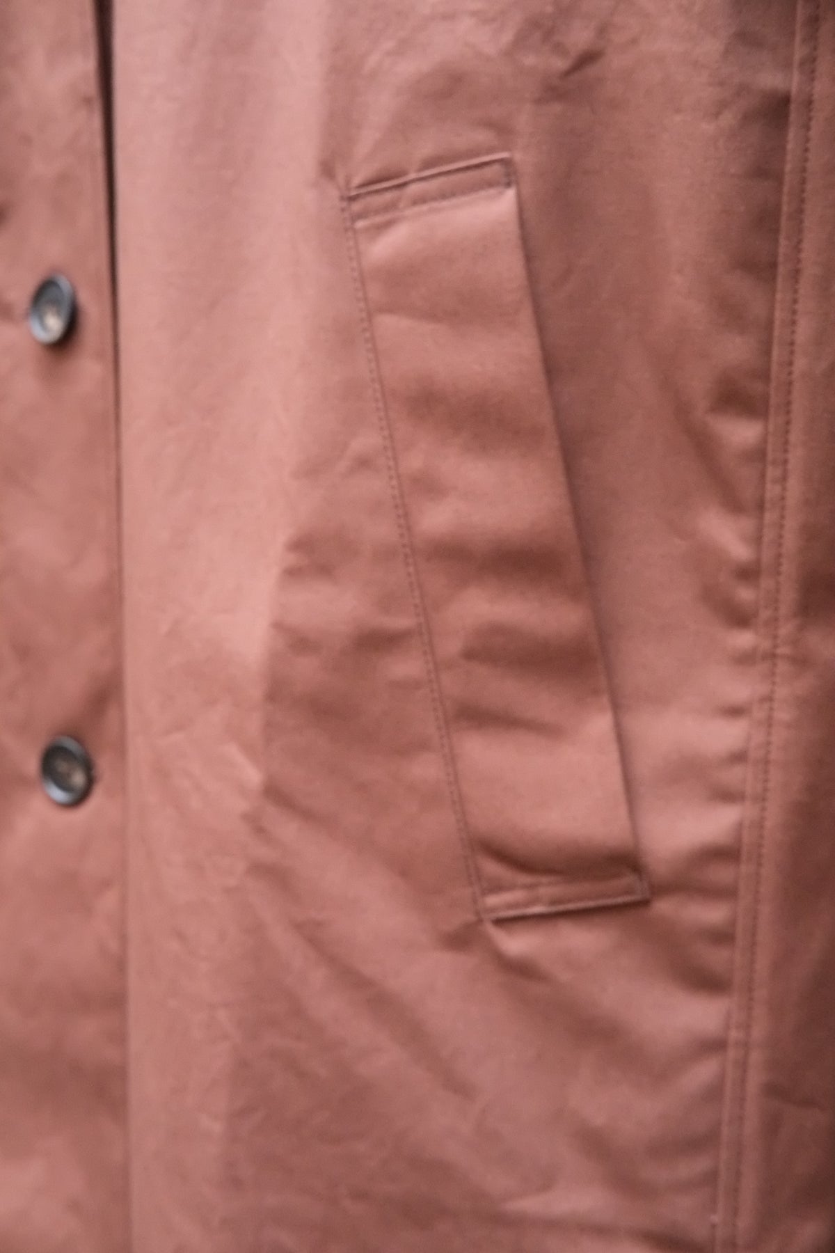 Close-up of a chocolate brown jacket fabric, showing a vertical welt pocket and part of a buttoned front closure.