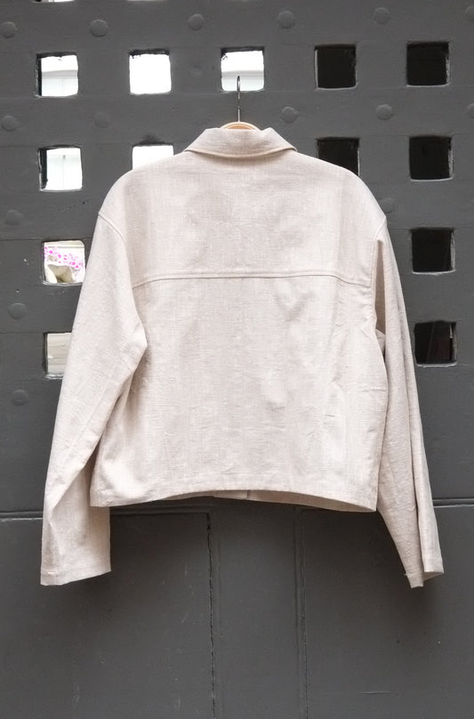 reverse of cropped jacket in a natural colour fabric photographed on a grey door