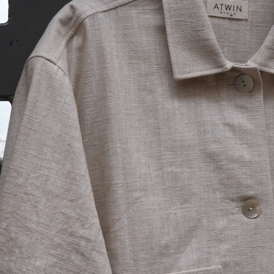 close up photo of a workwear style jacket with collar and shell buttons in a natural coloured fabric