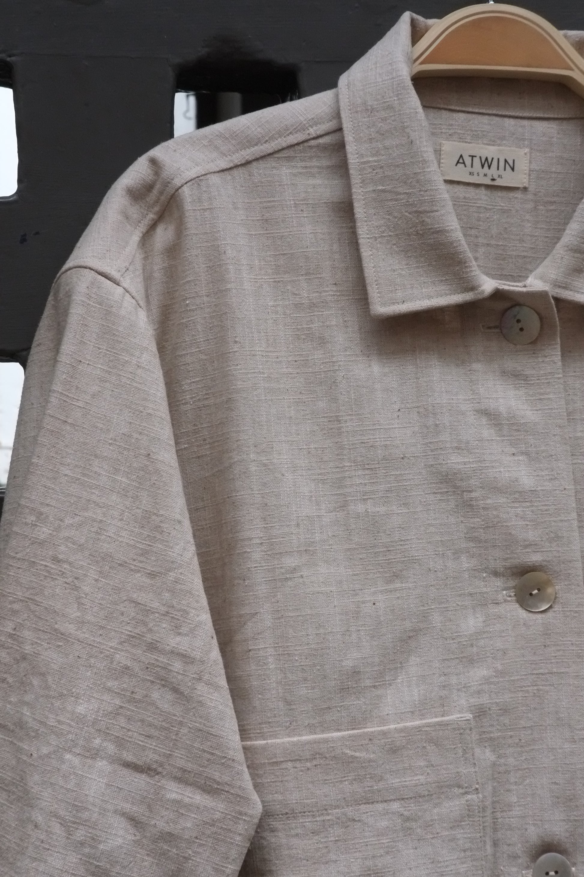 close up photo of a workwear style jacket with collar and shell buttons in a natural coloured fabric