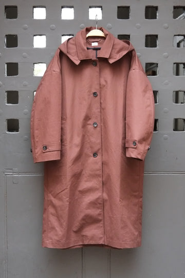 A chocolate brown hooded raincoat hanging on a wooden hanger against a grey door with a square grid pattern.