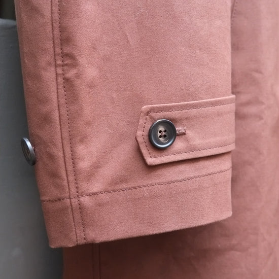 Close-up of a chocolate brown  jacket sleeve with a buttoned flap detail and visible fabric texture.