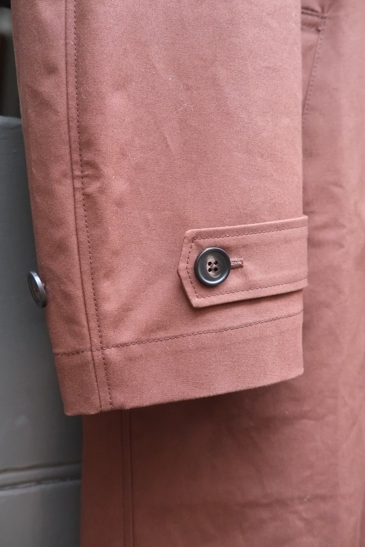 Close-up of a chocolate brown  jacket sleeve with a buttoned flap detail and visible fabric texture.