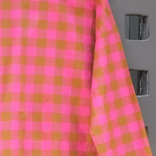 close up of pink and green checked long sleeve top pictures hanging on a wooden hanger on a grey door