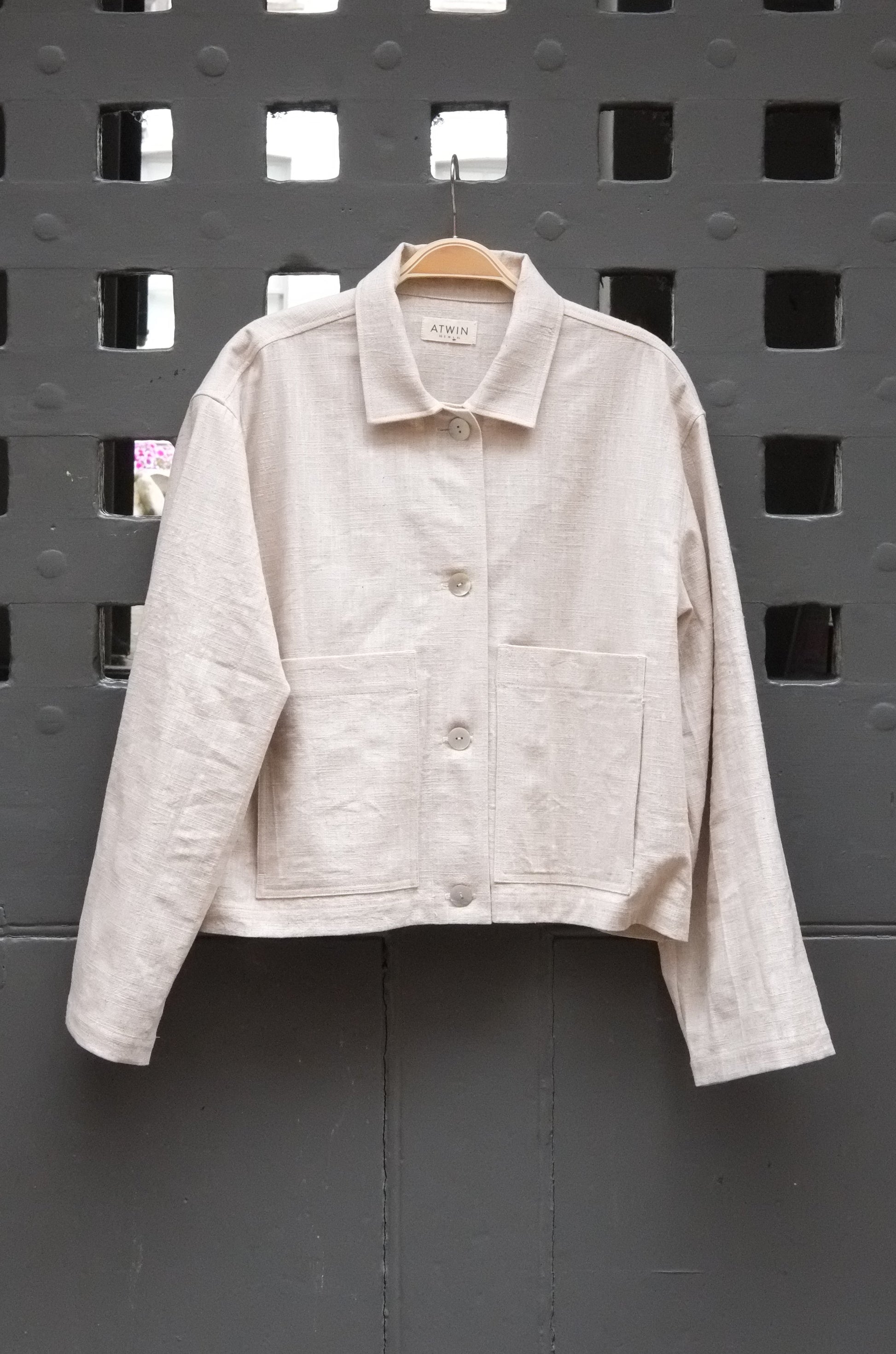 natural coloured workwear jacket with buttons photographed hanging on a grey door 