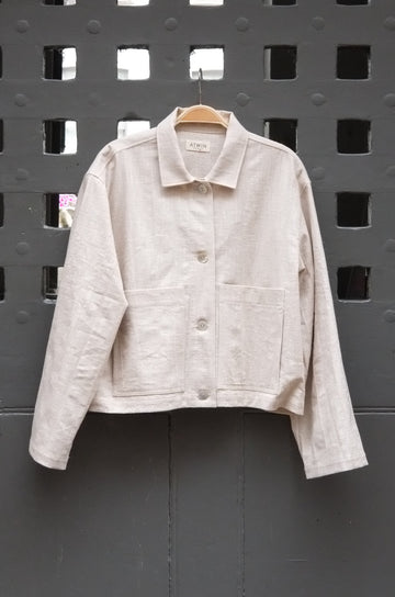 natural coloured workwear jacket with buttons photographed hanging on a grey door 