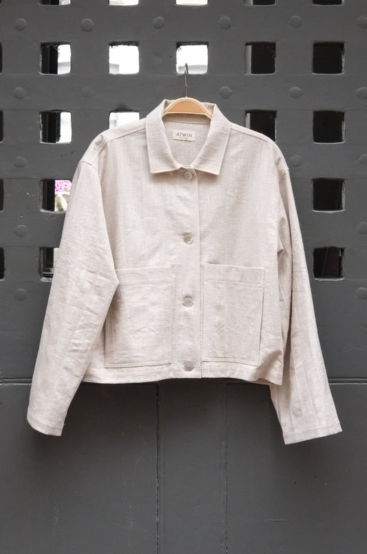 natural coloured workwear jacket with buttons photographed hanging on a grey door 