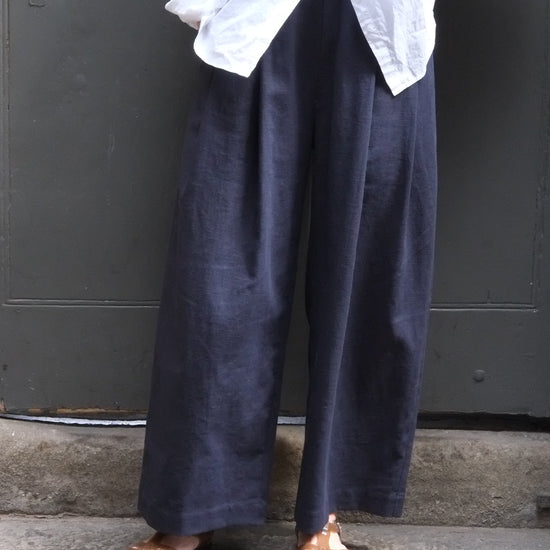 Person wearing dark pants and brown shoes standing on a concrete surface with a white garment.