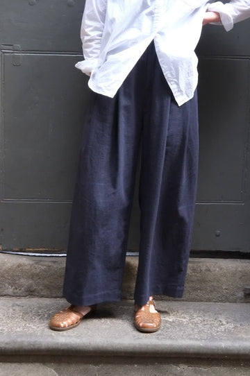 Person wearing dark pants and brown shoes standing on a concrete surface with a white garment.