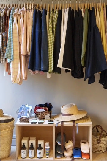 Clothing rack with various garments and a small display of shoes and bottles on a wooden shelf.