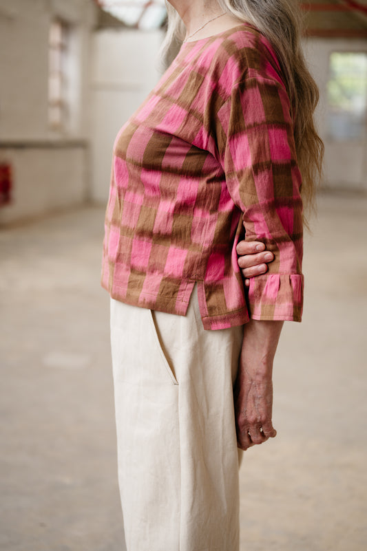Person wearing a pink and brown plaid shirt in an indoor setting