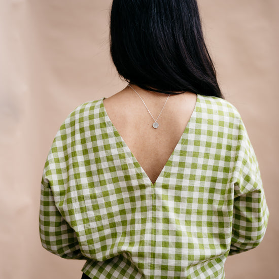Person wearing a green and white checkered blouse with a deep neckline on a beige background