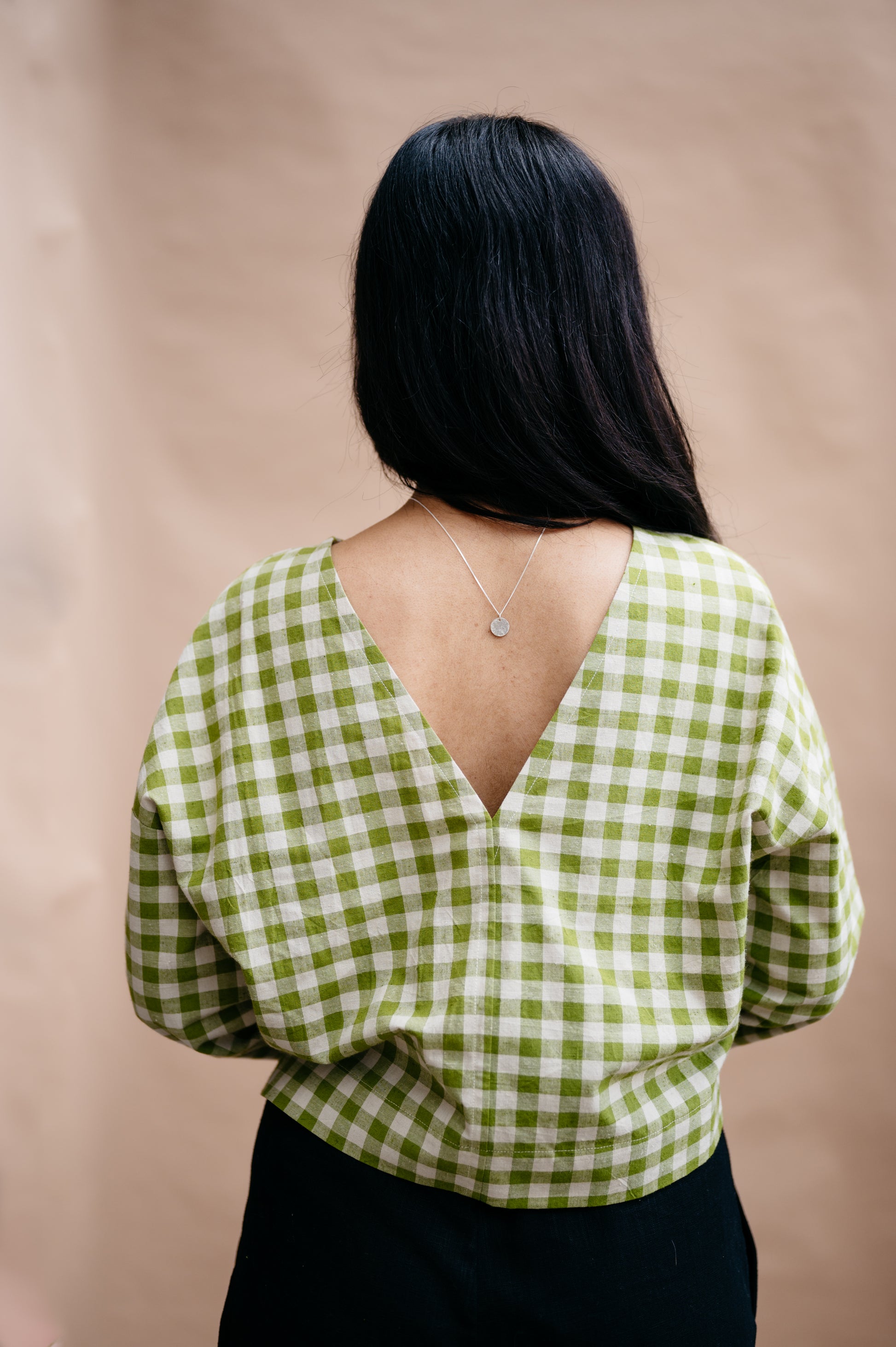 Person wearing a green and white checkered blouse with a deep neckline on a beige background