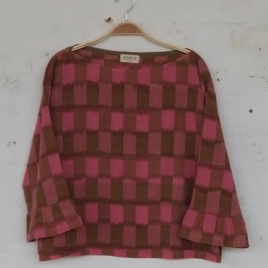 Pink and brown checkered shirt on a hanger against a white wall