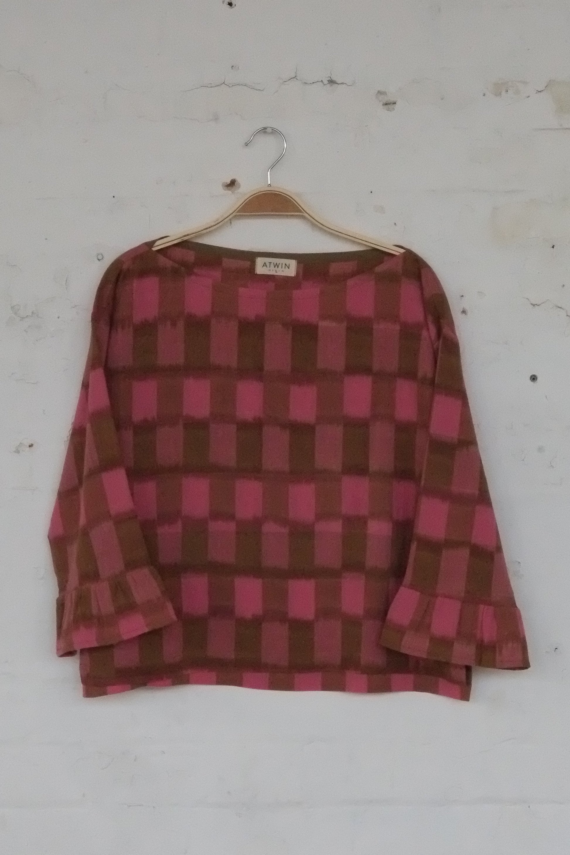 Pink and brown checkered shirt on a hanger against a white wall