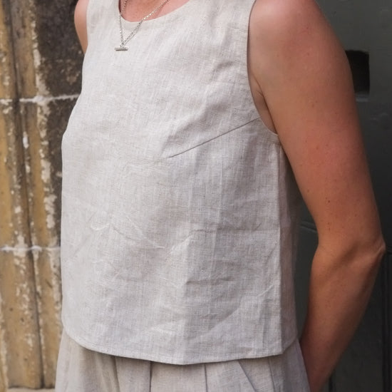 woman wearing a light-colored sleeveless top and trousers with pleated details.