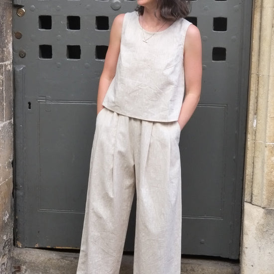 woman wearing a loose fitting cream coloured outfit with hands in pockets standing in front of an old door